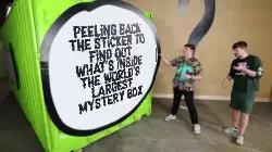 Peeling back the sticker to find out what's inside the world's largest mystery box meme
