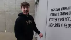 Mr Beast, tongue out and hoodie on, standing in front of the entrance gate, serious and playful at the same time meme