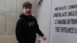 Mr Beast, tongue out and black sweater on, standing in front of the entrance gate meme